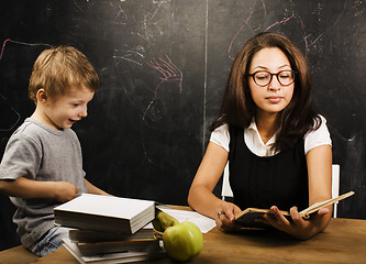 Image showing little cute boy with young teacher in classroom studying at blac