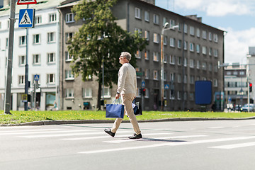 Image showing senior man with shopping bags walking on crosswalk