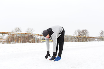 Image showing man exercising and stretching leg on winter bridge