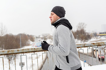 Image showing man in earphones running along winter bridge