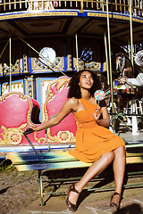 Image showing cool real african american teenage girl with candy near carousels at amusement park, lifestyle people concept