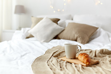 Image showing coffee cup and croissant on plaid in bed at home