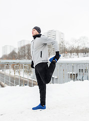 Image showing man exercising and stretching leg on winter bridge