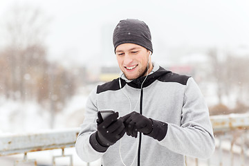 Image showing happy man with earphones and smartphone in winter