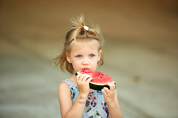 Image showing Adorable blonde girl eats a slice of watermelon outdoors.