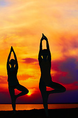 Image showing Yoga people training and meditating in warrior pose outside by beach at sunrise or sunset.