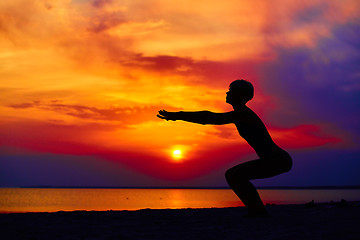 Image showing Silhouette of woman standing at yoga pose on the beach during an amazing sunset