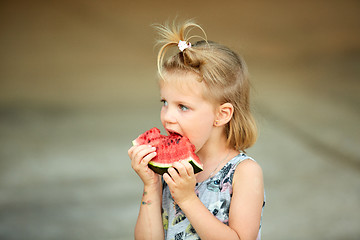 Image showing Adorable blonde girl eats a slice of watermelon outdoors.