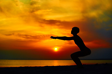 Image showing Silhouette of woman standing at yoga pose on the beach during an amazing sunset