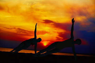 Image showing Yoga people training and meditating in warrior pose outside by beach at sunrise or sunset.