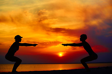 Image showing Yoga people training and meditating in warrior pose outside by beach at sunrise or sunset.