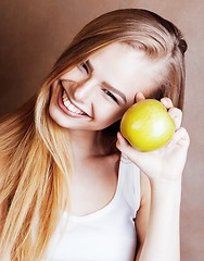 Image showing young pretty blond woman with green apple happy cheerful smiling close up on warm brown background, lifestyle people concept