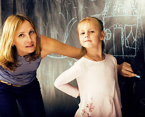 Image showing portrait of mature woman teacher with little cute blonde girl pupil writing on blackboard together, lifestyle people concept