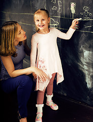 Image showing portrait of mature woman teacher with little cute blonde girl pupil writing on blackboard together, lifestyle people concept