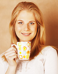 Image showing young cute blond girl drinking coffee close up on warm brown bac