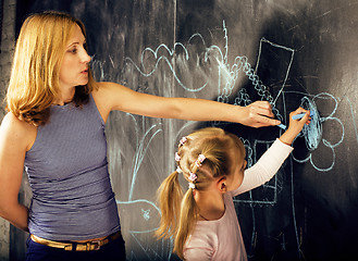 Image showing portrait of mature woman teacher with little cute blonde girl pupil writing on blackboard together, lifestyle people concept