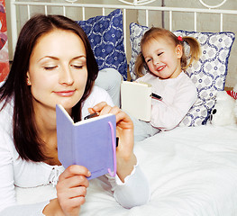 Image showing portrait of mother and daughter laying in bed  reading and writi