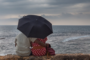 Image showing Rear View of Indian couple sitting by sea with an umbrella looking at horizon.