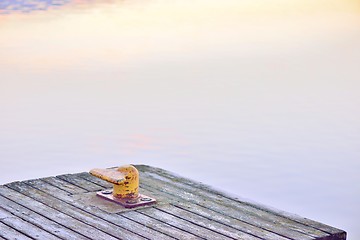 Image showing Yellow bollard, or a harbor post, on a wooden pier.