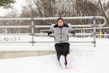 Image showing sports man doing triceps dips at fence in winter