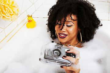 Image showing young afro-american teen girl laying in bath with foam, wearing 