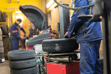 Image showing Professional auto mechanic replacing tire on wheel in car repair service.