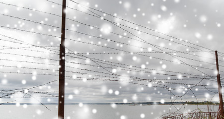 Image showing broken barb wire fence over gray sky and sea