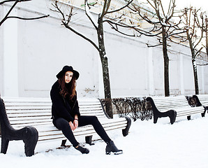 Image showing young pretty modern hipster girl waiting on bench at winter snow park alone, lifestyle people concept