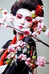 Image showing young pretty geisha in black kimono among sakura, asian ethno