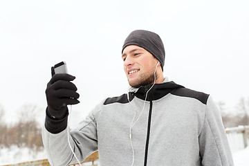 Image showing happy man with earphones and smartphone in winter