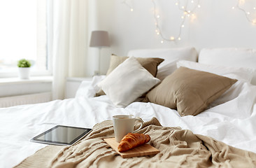 Image showing tablet pc, coffee cup and croissant on bed at home