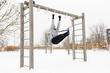 Image showing young man exercising on horizontal bar in winter