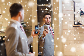 Image showing man in suit taking mirror selfie at clothing store