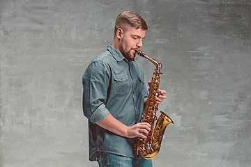 Image showing Happy saxophonist playing music on sax over gray background