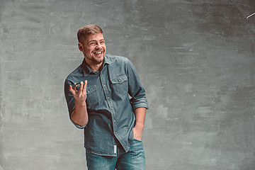 Image showing The young smiling caucasian businessman on gray background with phone