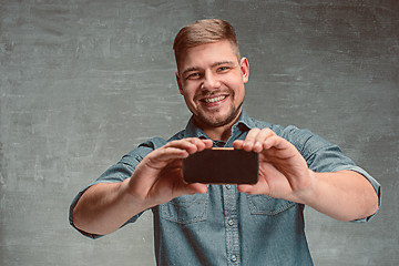 Image showing The young smiling caucasian businessman on gray background with phone