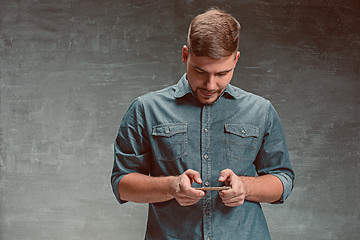 Image showing The young smiling caucasian businessman on gray background with phone