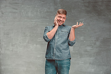 Image showing The young smiling caucasian businessman on gray background talking with phone