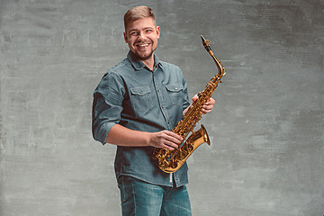 Image showing Happy saxophonist with sax over gray background