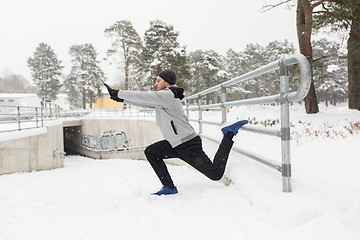 Image showing sports man stretching leg at fence in winter