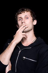 Image showing The young man smokes a cigarette. Isolated on a black background