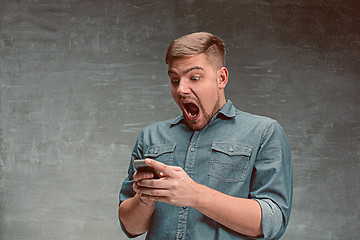 Image showing The young smiling caucasian businessman on gray background with phone