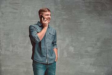 Image showing The young smiling caucasian businessman on gray background talking with phone