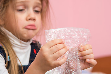 Image showing Upset girl pouting cheeks eats bubbles packaging film