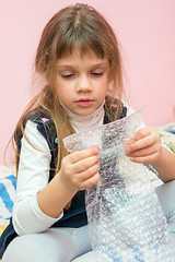 Image showing Five-year girl sitting on the bed and eats bubbles packaging package