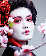 Image showing young pretty geisha in black kimono among sakura, asian ethno