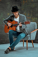 Image showing Cool guy with hat playing guitar on gray background