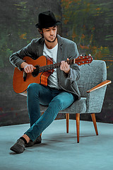 Image showing Cool guy with hat playing guitar on gray background