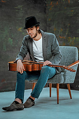 Image showing Cool guy sitting with guitar on gray background