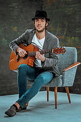 Image showing Cool guy with hat playing guitar on gray background